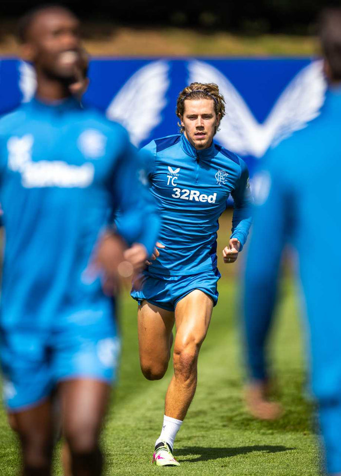 Athlete in blue Rangers training top sprinting on a field with 32Red sponsor logo visible