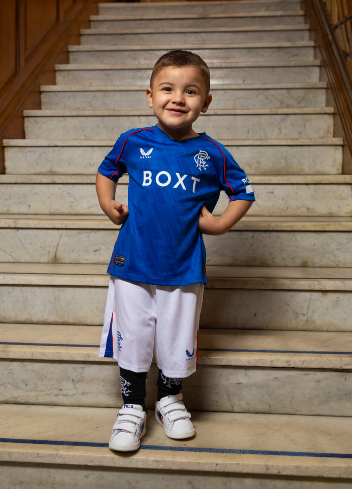 Smiling toddler in blue Rangers infant home kit on stairs