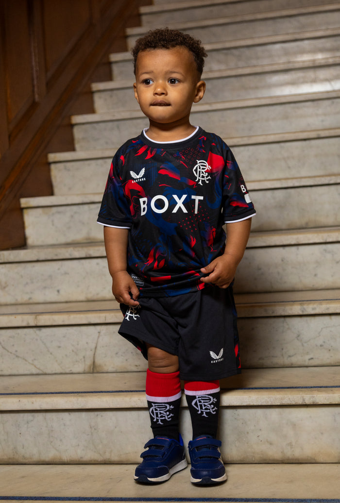 Young child wearing the Infant Rangers Third Nested Short Sleeve Kit with black shorts and red socks on stairs