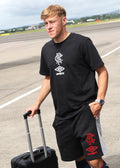 Front view of black Unisex travel shorts on a model, displaying red Umbro crest and diamond logo on the leg