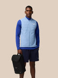 Model wearing a light blue padded vest holds a black boot bag.