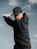 Athlete in black Golf Pinnacle Performance Hoodie with hood up mid swing holding a golf club outdoors