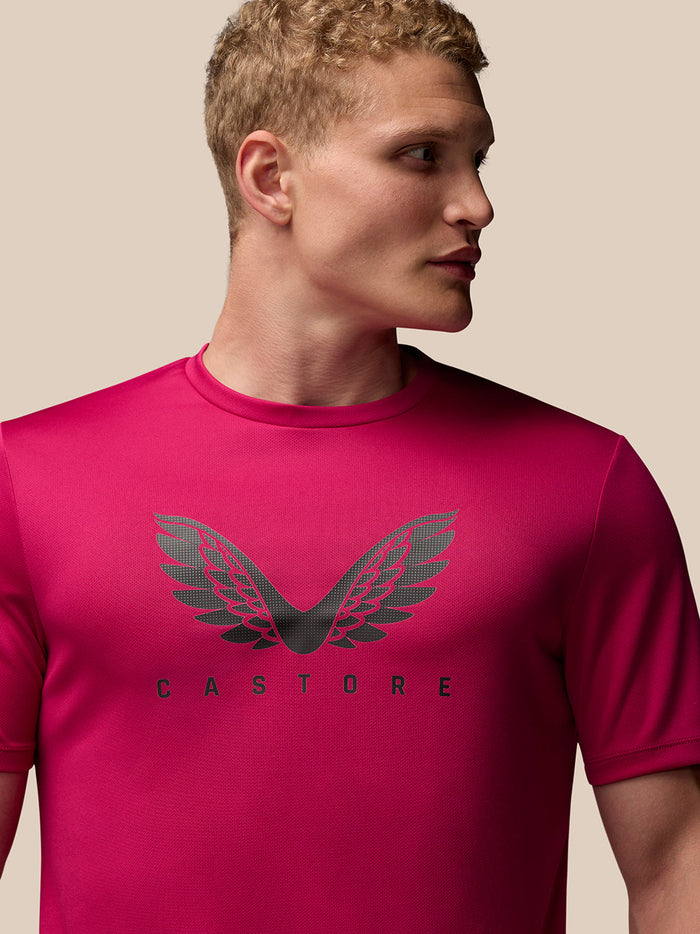 Male model wearing pink Adapt Training T Shirt with a wing graphic on the chest against a beige background.
