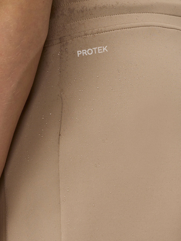 Close-up of beige fabric showing PROTEK logo and water droplets, highlighting water resistance.