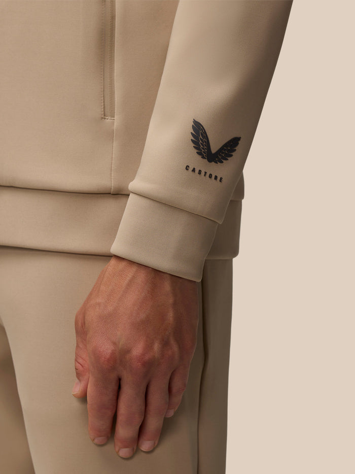 Beige quarter zip top close up showing Castore wordmark on chest.