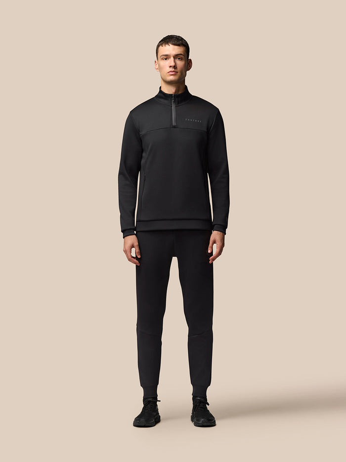 Full-body view of a male model in a black Castore tracksuit with a quarter-zip top and matching joggers
