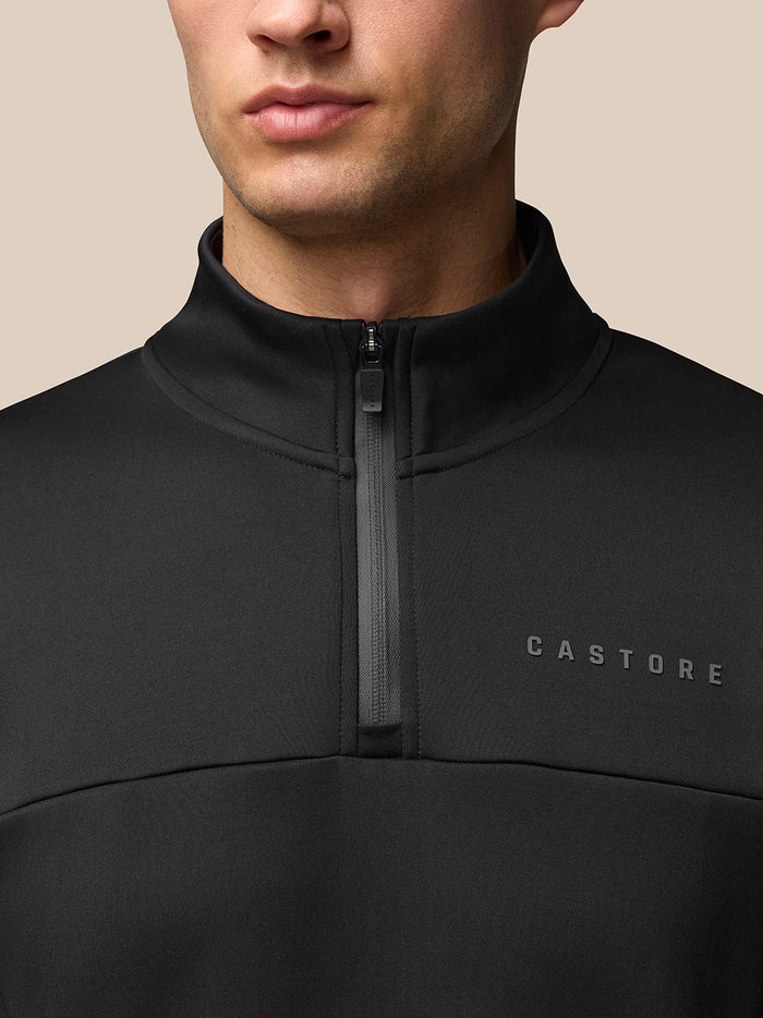 Close-up of a male model wearing a black quarter-zip top with a centered zipper and Castore logo on the chest