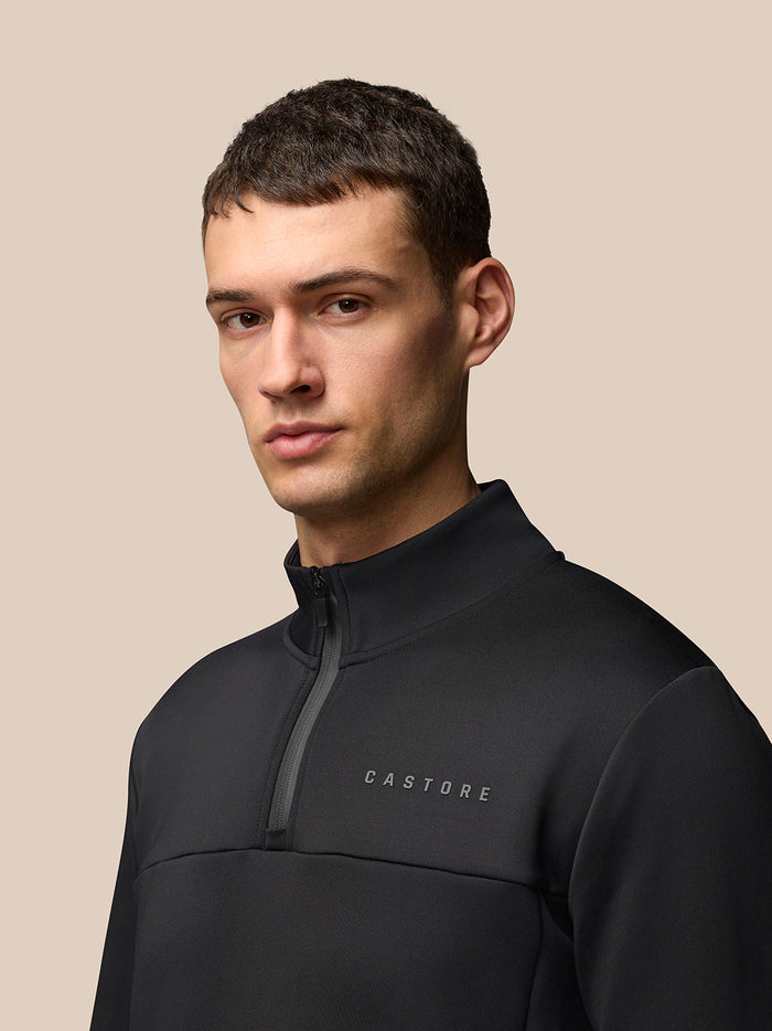 Close-up of a male model wearing a black FLEX LIFESTYLE 1/4 ZIP top with high collar and Castore branding on the chest