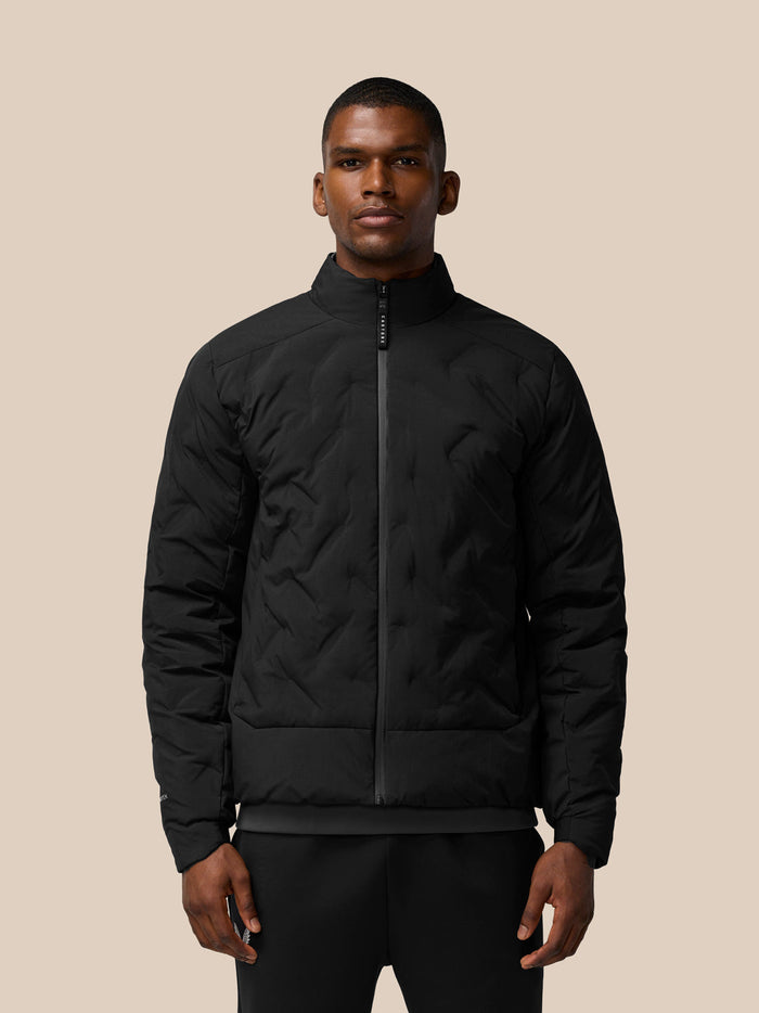 Male model wearing black padded jacket with stand collar and front zip; zip pockets, Castore branding on left shoulder and Protek branding on right sleeve