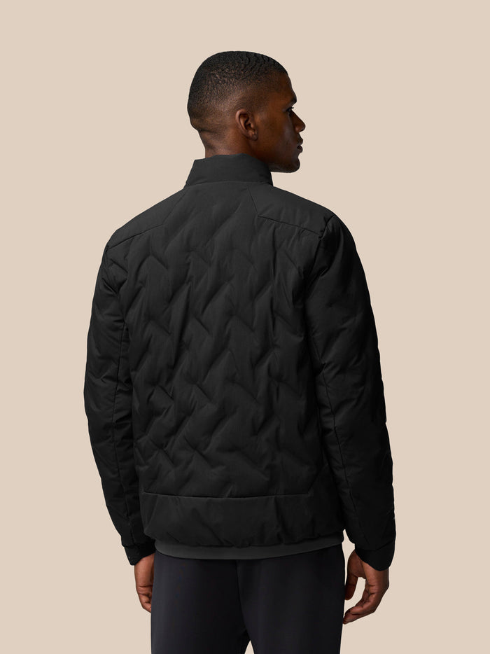 Back view of a man wearing a black padded jacket with a quilted chevron pattern and stand collar.