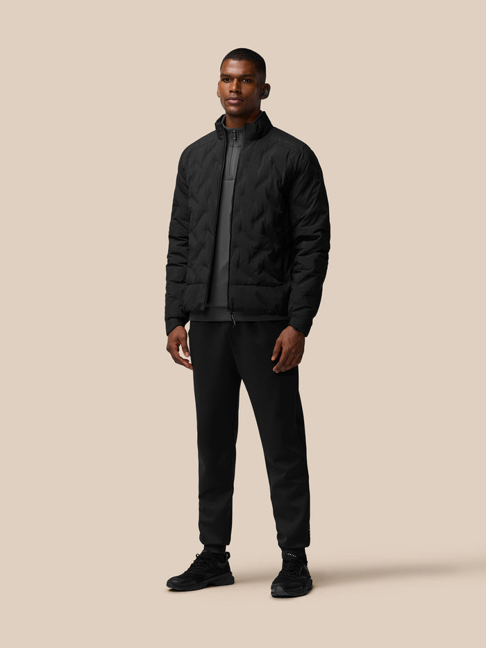 Full-length portrait of a man in a black padded jacket with stand collar and zip front.