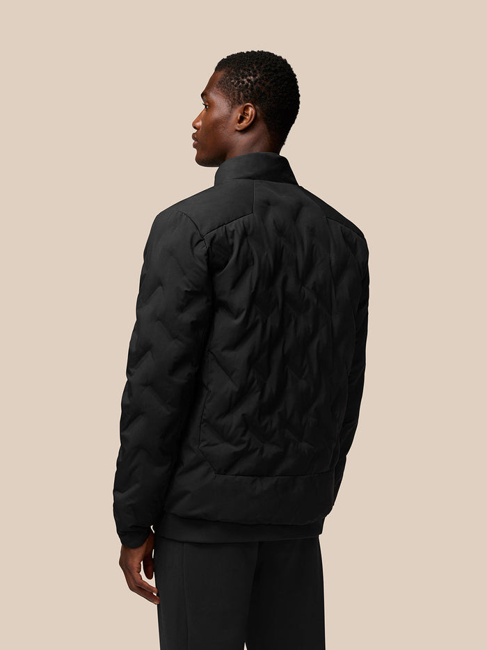 Back view of black padded jacket on model showing quilted panels and stand collar