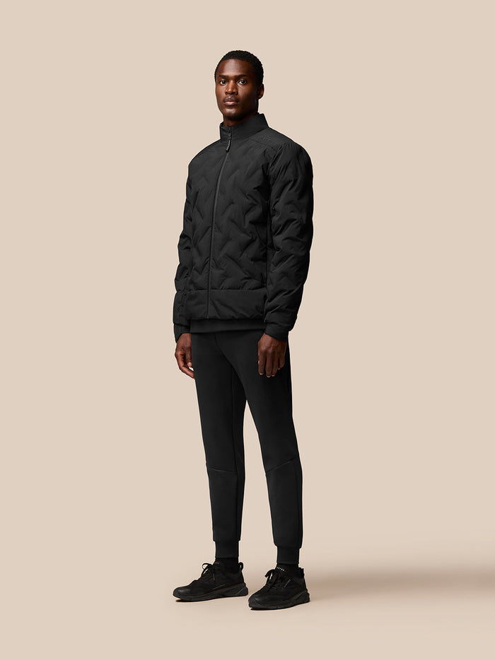 Male model wearing a black padded jacket with stand collar and full front zipper.