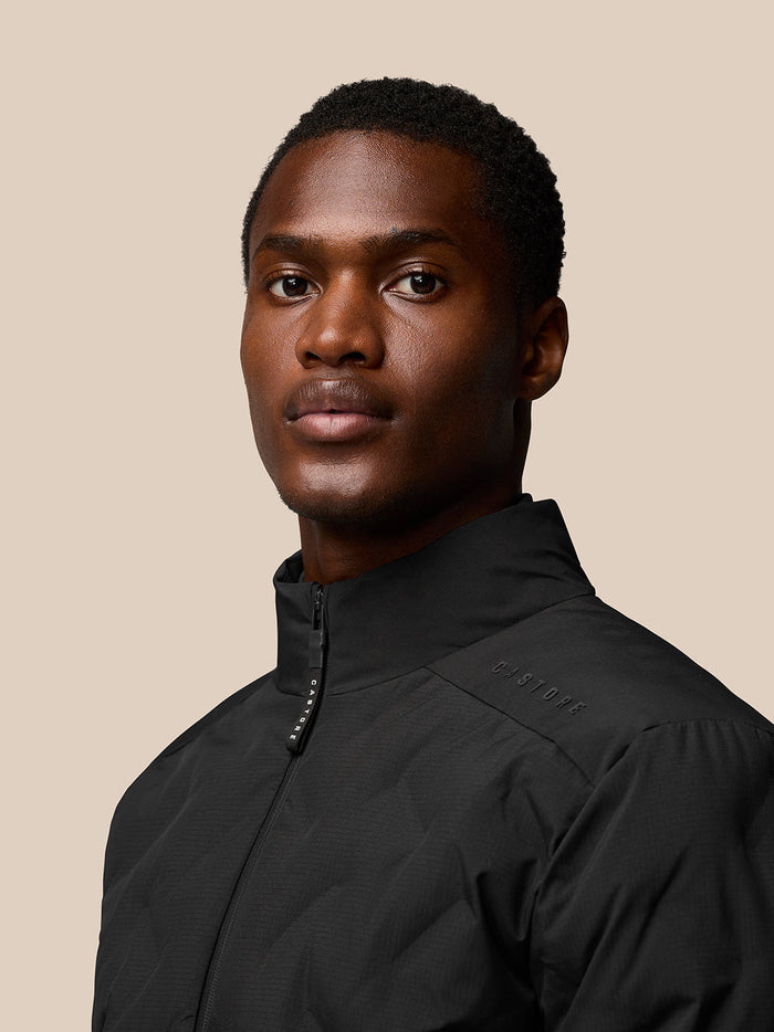 Black padded jacket close up with stand collar and Castore branding on the shoulder.