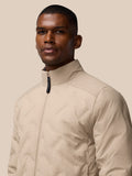 Portrait of a man wearing a beige padded jacket with a zip front and high collar against a neutral background