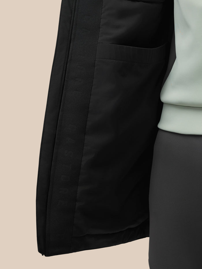 Close-up of the black longline jacket showing a front zipper and PROTEK branding on the sleeve