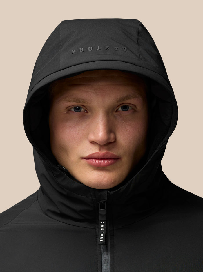 Portrait of a model wearing a black Castore longline padded jacket with hood up and front zipper