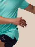 Model wearing light aqua Zone Training T-Shirt with a chest logo and navy shorts against a beige background.