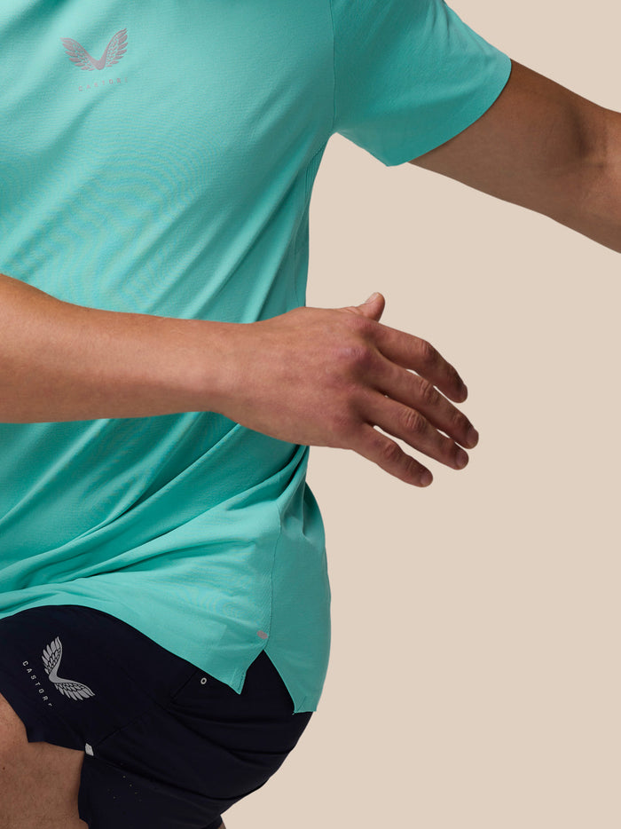 Model wearing light aqua Zone Training T-Shirt with a chest logo and navy shorts against a beige background.