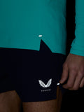 Side view of teal Zone Training top with vented hem worn over navy shorts Castore logo on shorts