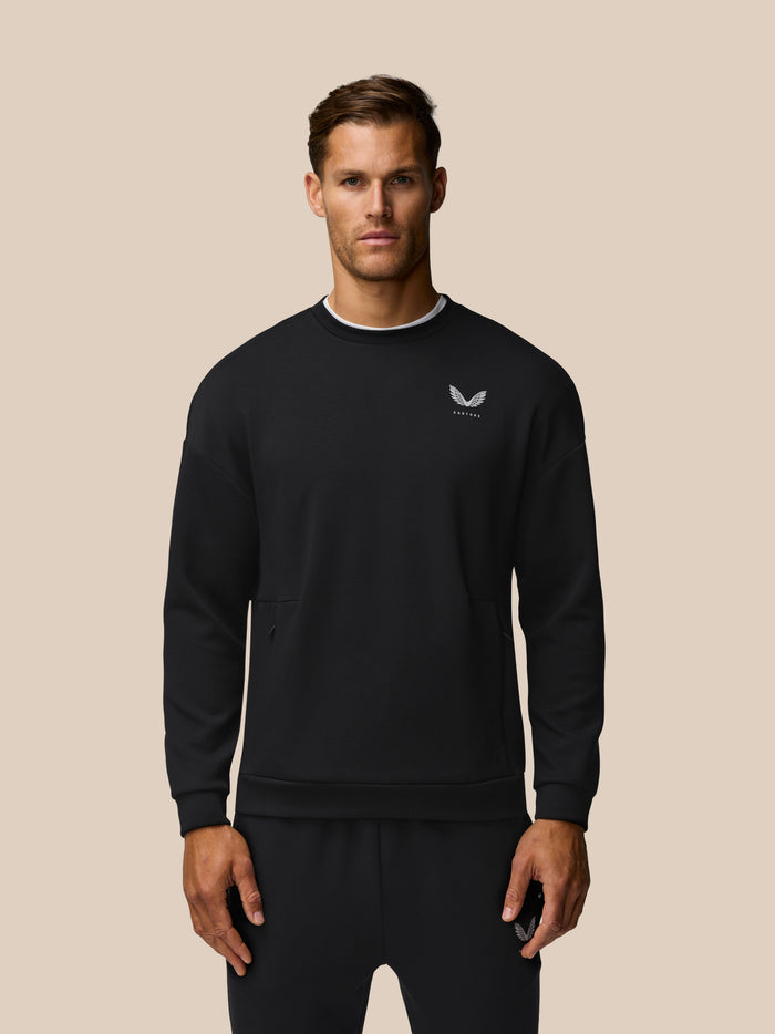 Male model wearing black crew neck travel lifestyle sweatshirt with small chest logo and white neckline visible