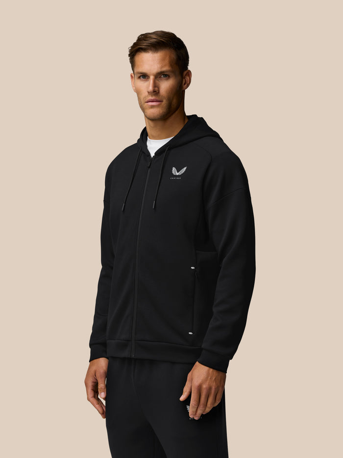 Man wearing black travel lifestyle zip hoodie with hood down and Castore logo on chest
