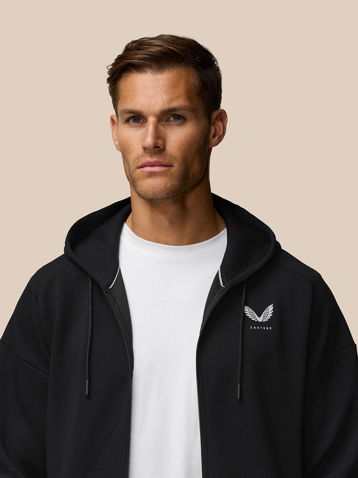 Male model in black travel zip hoodie with drawstring hood and left chest Castore logo over a white tee.