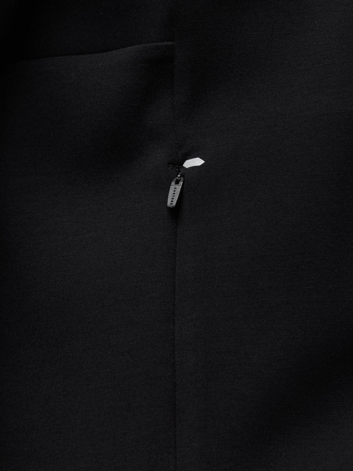 Close up of black travel hoodie fabric with a metal zipper pull and a white reflective patch.