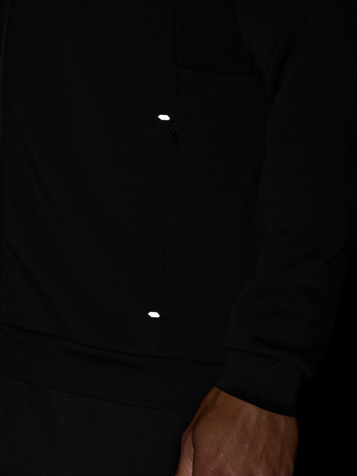 Close up of black zip hoodie front with a metal zipper and a small white reflective patch near the zip.
