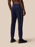 Back view of a male model wearing navy Flex Thermo Pant with a black side stripe and black sneakers.