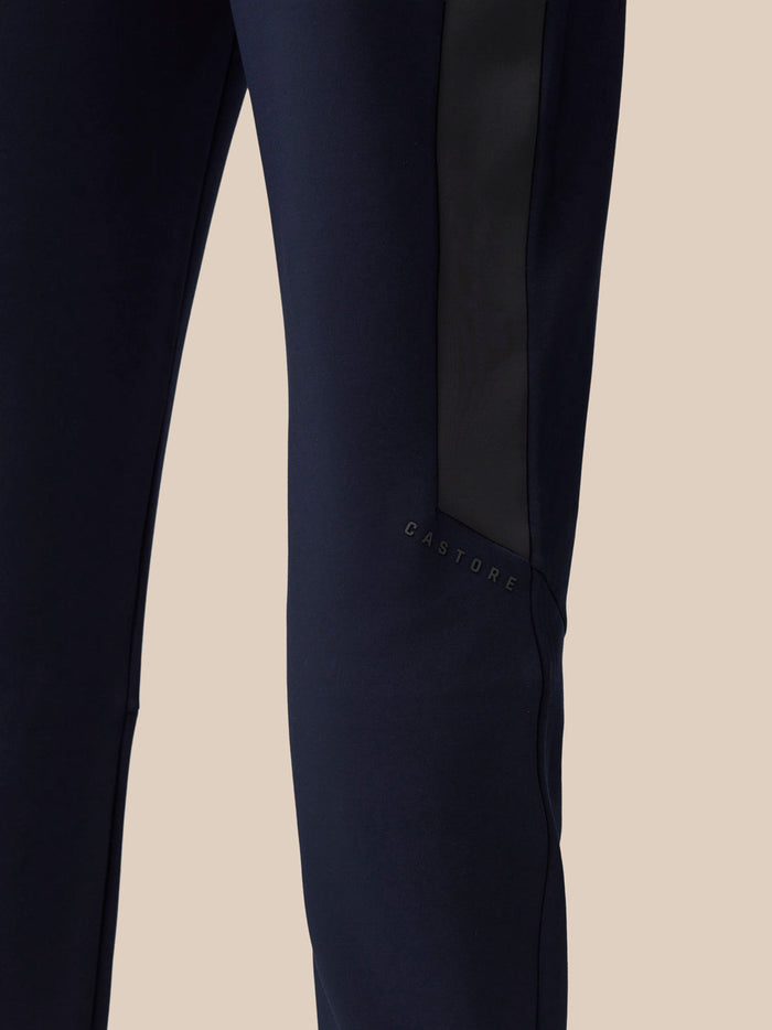 Close-up of a navy pant leg showing a black side panel and Castore branding along the seam.