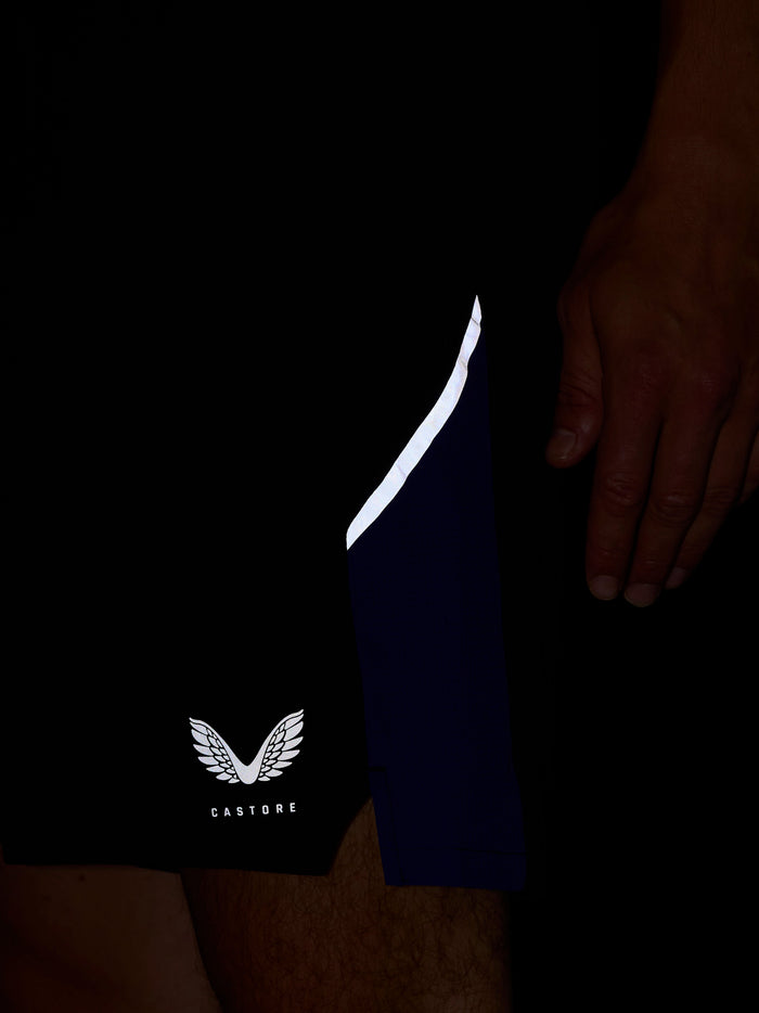 Close up of navy shorts with a white side stripe and Castore wing logo at the hem against a dark background