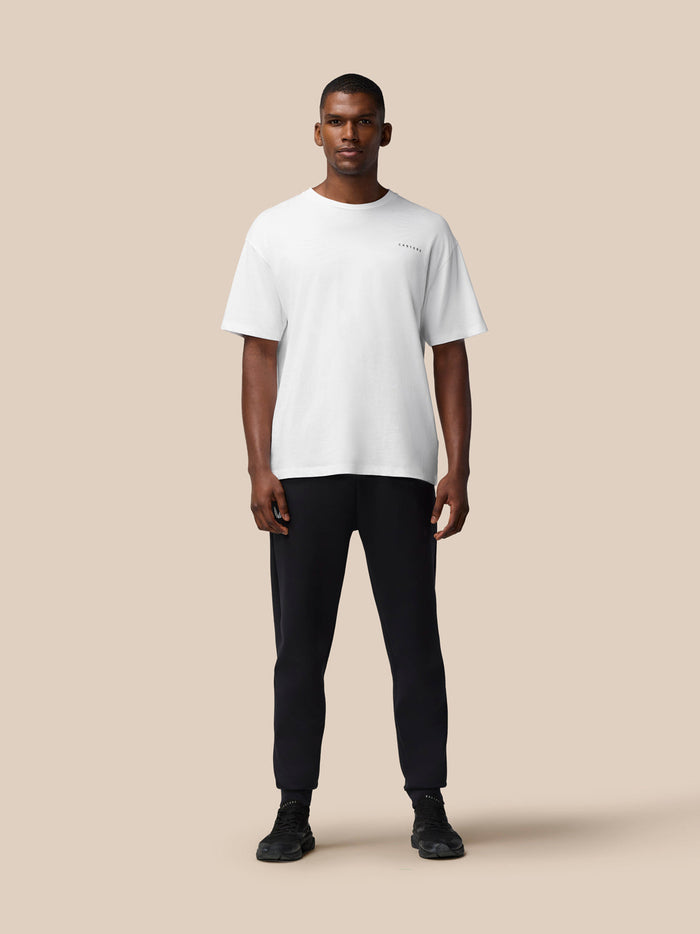 Full-body view of a man wearing a white flex cotton short sleeve T-shirt with a round neckline against a beige background.