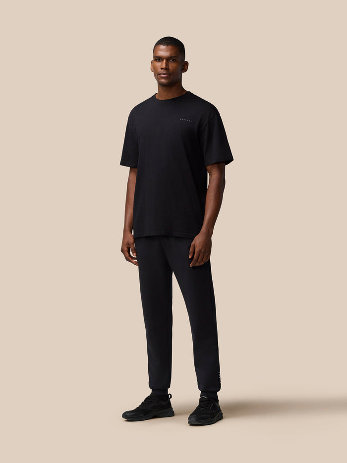 Full body view of a man wearing a black T shirt and matching joggers with black sneakers
