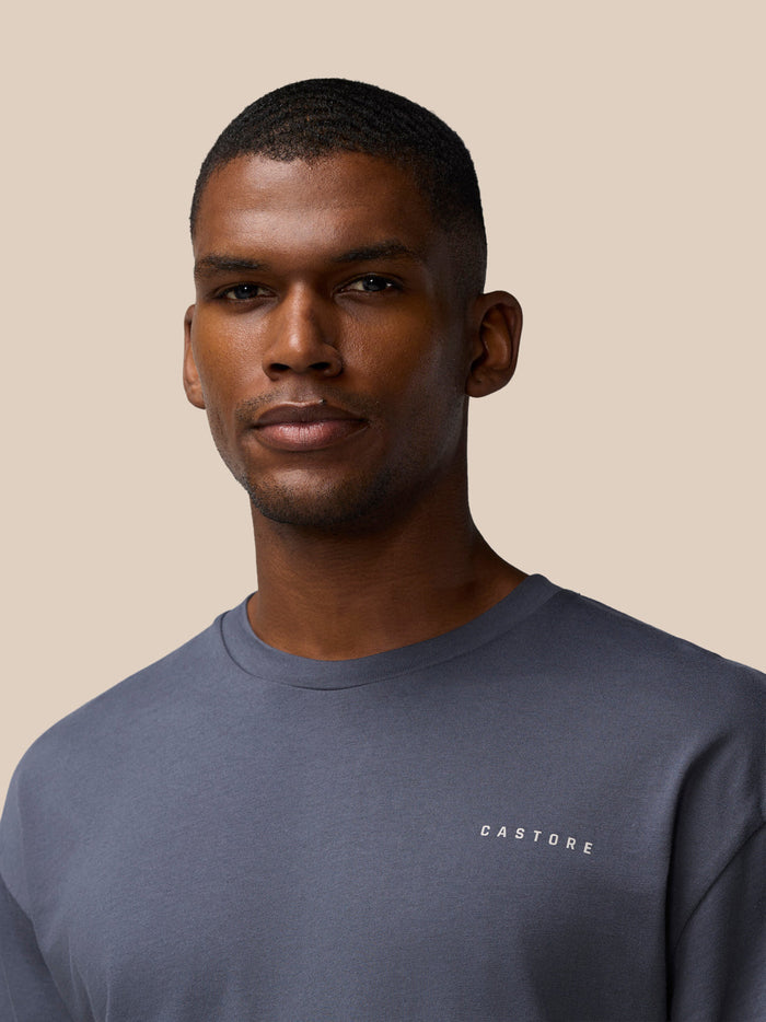 Close up of a man wearing a pewter colored Castore crew neck cotton T shirt.