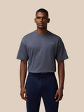 Male model wearing a pewter gray flex T shirt with a small chest logo and navy drawstring shorts against a beige backdrop