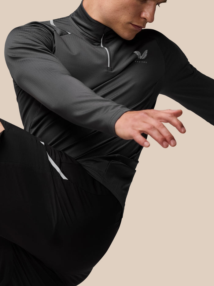 Charcoal Apex Training Winterised ¼ zip top on a model with reflective zipper detail and Castore wing logo on the chest