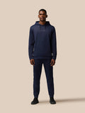Full-body shot of a man wearing navy Flex Thermo Hoodie and joggers with Castore branding on chest.