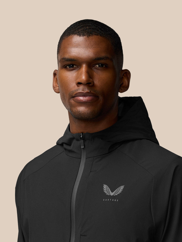 Portrait of a man in a black hooded Flex Winterised woven jacket with front zipper and Castore logo on the chest