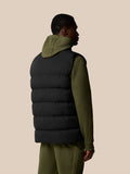 Back view of black sleeveless puffer gilet layered over olive green hoodie.