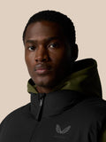 Close up of a man wearing a black hooded puffer gilet with olive lining and logo on the chest.