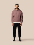 Male model wearing mauve ADAPT LIFESTYLE HOODIE with front kangaroo pocket, full body shot against beige background.