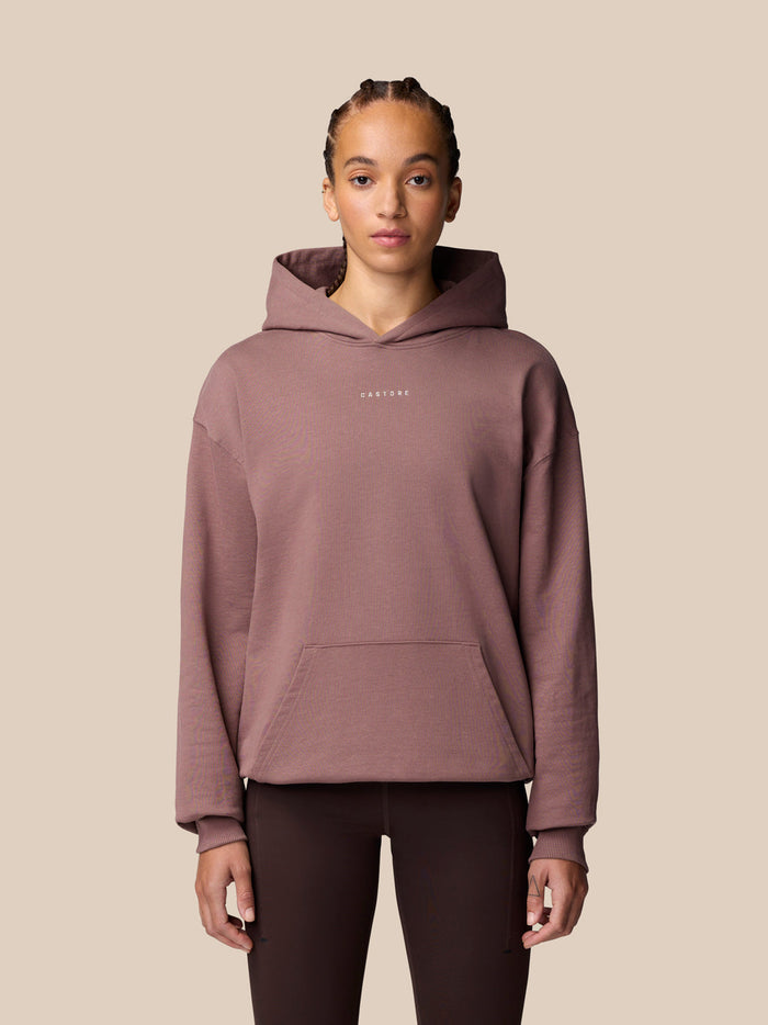 Female model wearing a mauve hoodie with a front kangaroo pocket and small logo on the chest