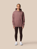 Female model in mauve ADAPT LIFESTYLE HOODIE with hood up and front pocket, full body shot against beige backdrop.