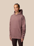 Close-up of female model wearing mauve ADAPT LIFESTYLE HOODIE with hood against beige background.