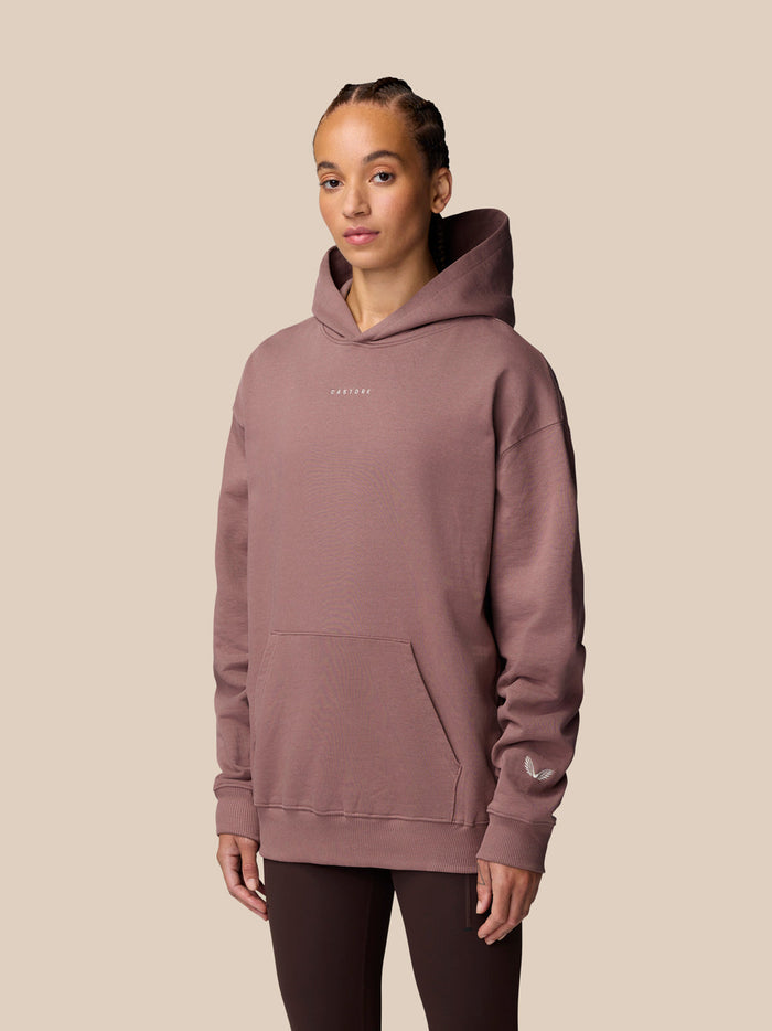 Close-up of female model wearing mauve ADAPT LIFESTYLE HOODIE with hood against beige background.