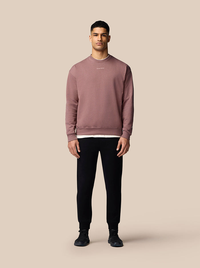 Full body shot of a male model wearing a mauve oversized ADAPT lifestyle sweatshirt with a left sleeve Castore wings logo.