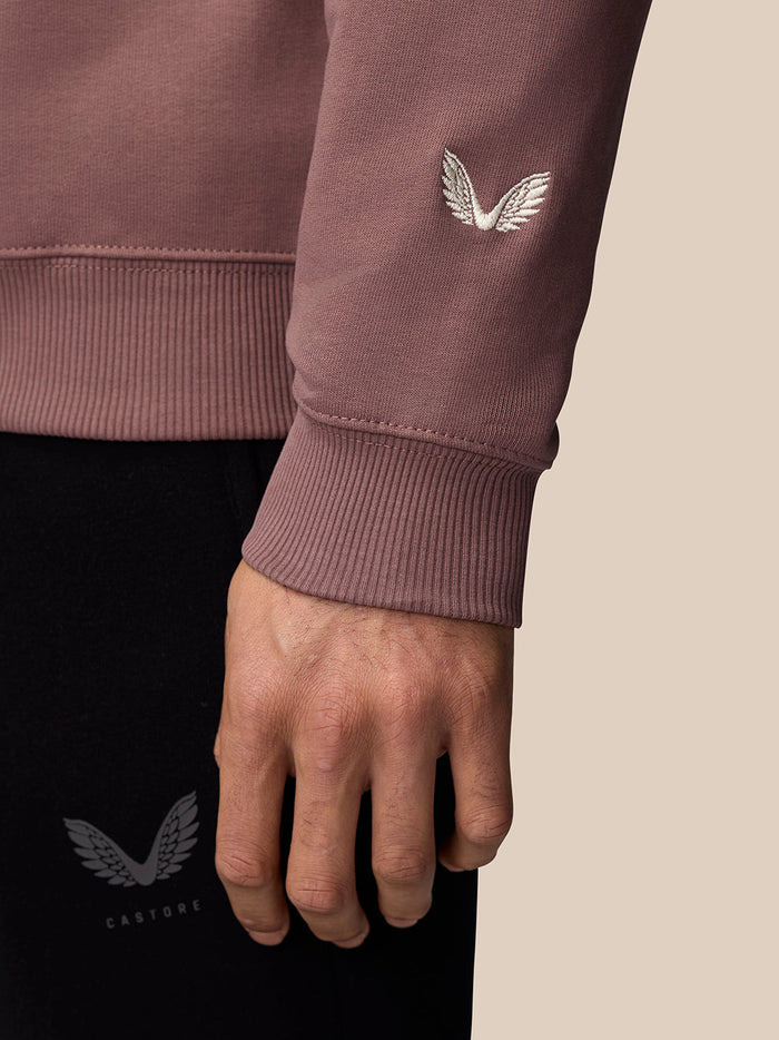 Close-up of mauve sweatshirt sleeve with the white embroidered Castore wings logo