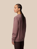 Back view of a mauve ADAPT lifestyle sweatshirt on a model with a wing logo on the left sleeve.