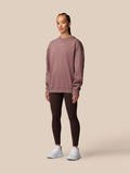 Female model wearing mauve ADAPT LIFESTYLE SWEATSHIRT with oversized fit and crew neckline, paired with dark leggings